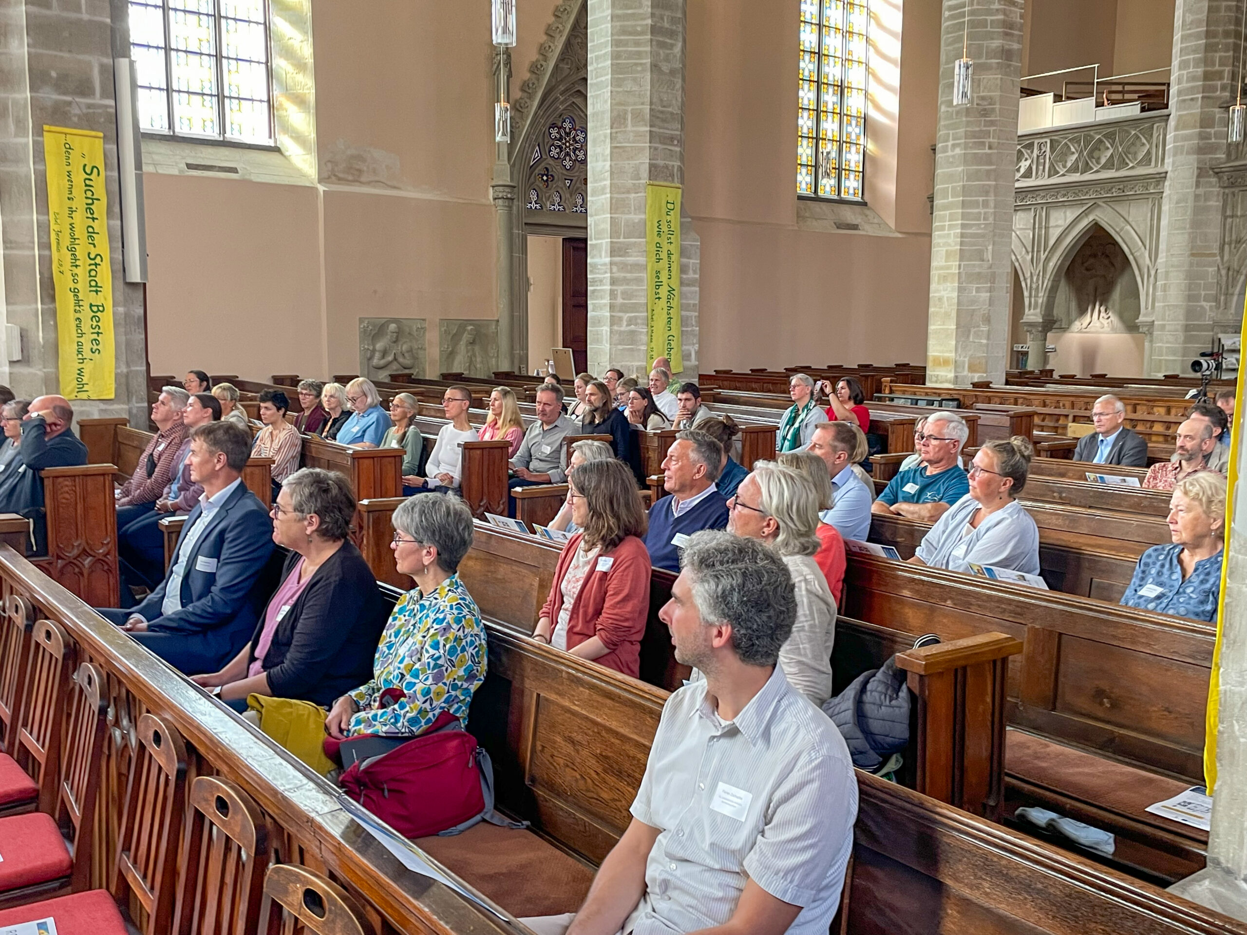 Menschen in Kirchenbänken, die einem Vortrag lauschen.